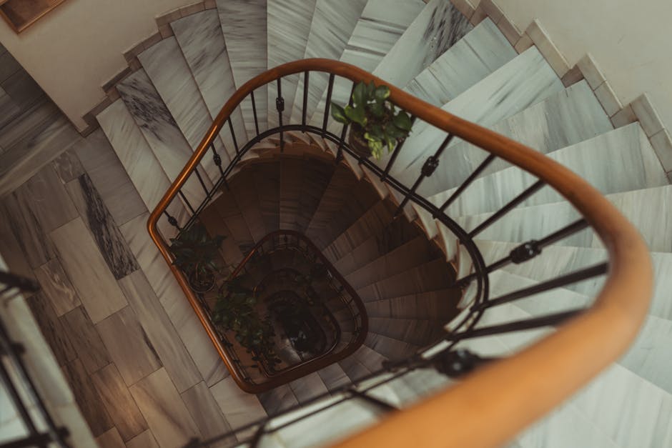 The image shows a view from the top of a staircase inside a home, leading down to a small landing area. The staircase has white marble steps with grey veining, and the walls on either side are decorat